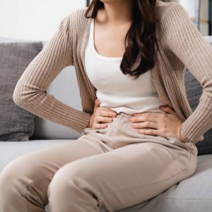 The woman with a stomachache is holding her stomach in pain, sitting on the sofa in the living room. she is suffering from a stomachache. Healthcare and medical concept.